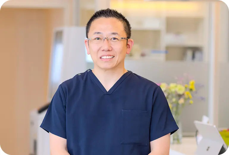 田岡歯科・矯正歯科クリニック院長のプロフィール写真｜紺色の診療衣を着用