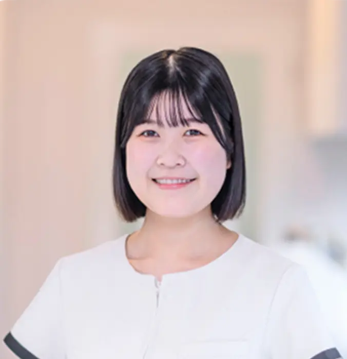 笑顔で前を向く白い制服を着た女性スタッフのポートレート。歯科医院のスタッフインタビュー。