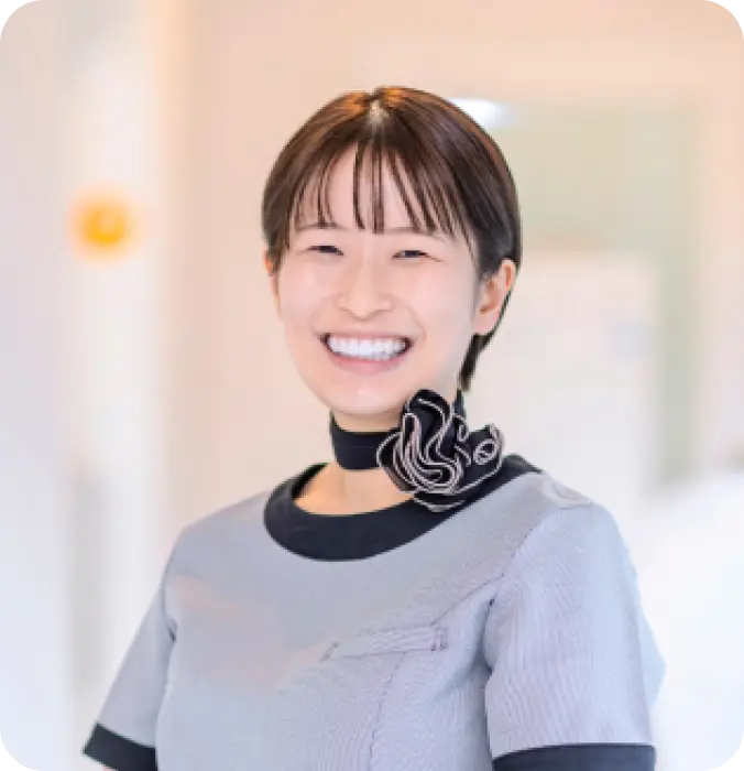 グレーの制服とスカーフを着用した女性スタッフの満面の笑み。歯科医院で働くスタッフの紹介写真。